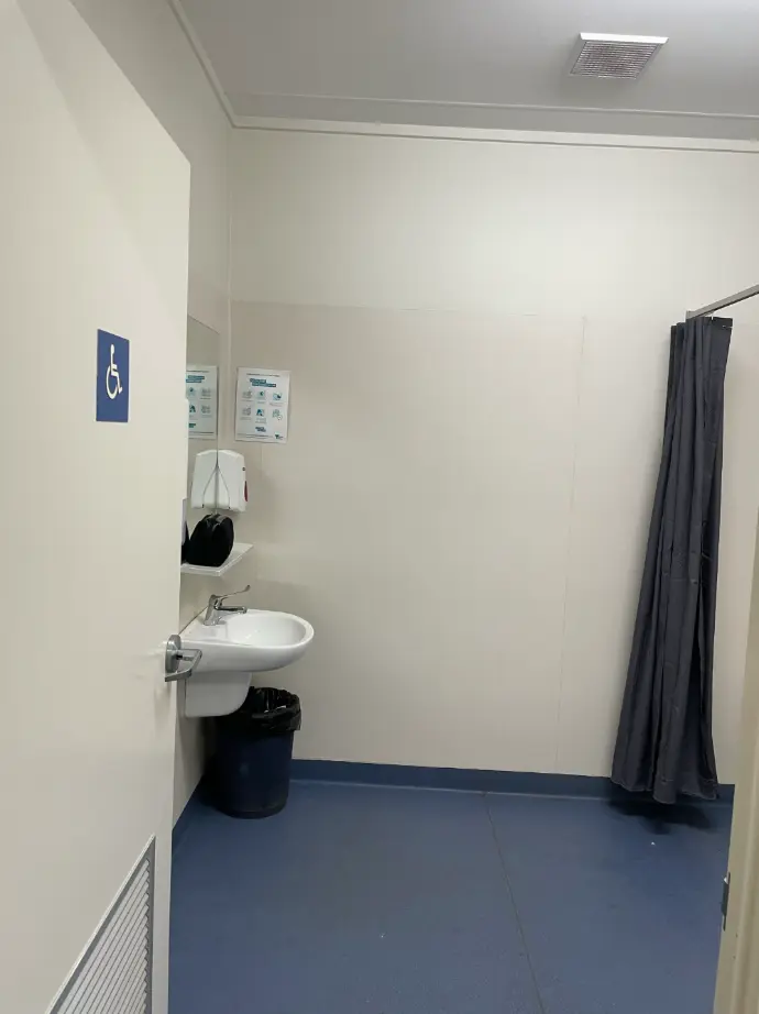 Picture of the Accessible Bathroom through the doorway, showing the sink, open space and part of the open shower curtain around the roll in shower.