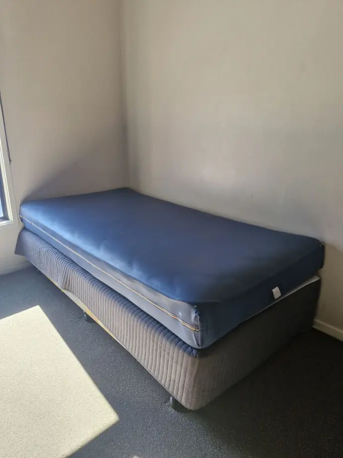 Image shows a King Single bed, with a waterproof mattress protector on the mattress atop a bedframe with lockable wheels - Easily moved around the room if required.