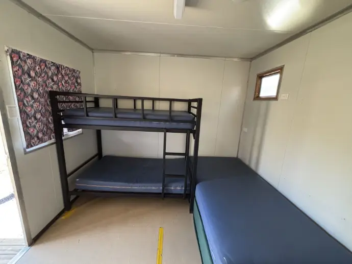 Image shows a bunk and King single bed arranged inside a small room, with two windows - one with curtains drawn, and the other window uncovered..